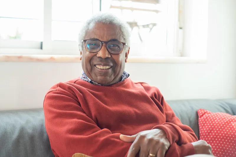 An older man smiling on a sofa at home