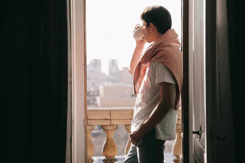 A man standing at an open balcony door with a coffee